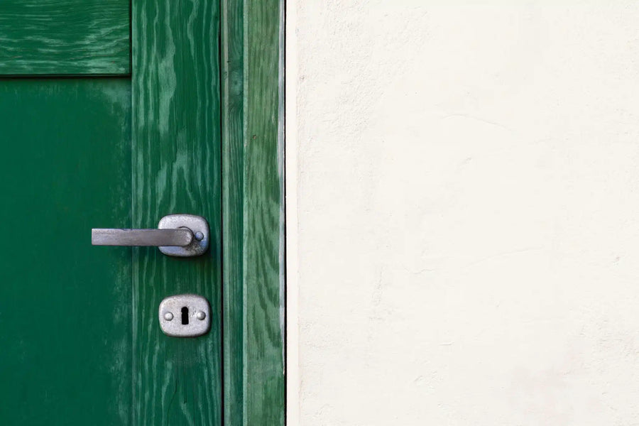 Green door with metal handle against white wall