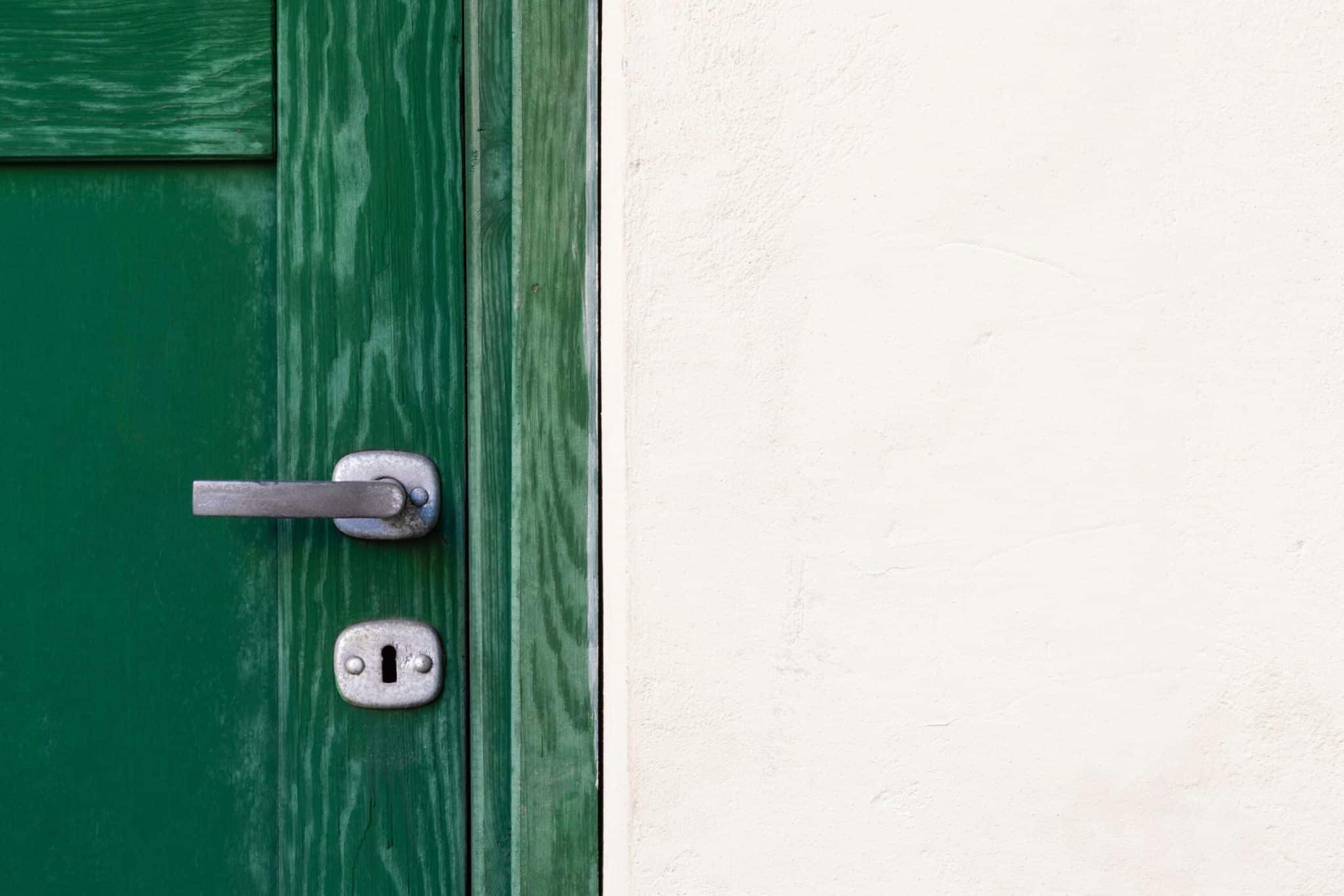 Green door with metal handle against white wall